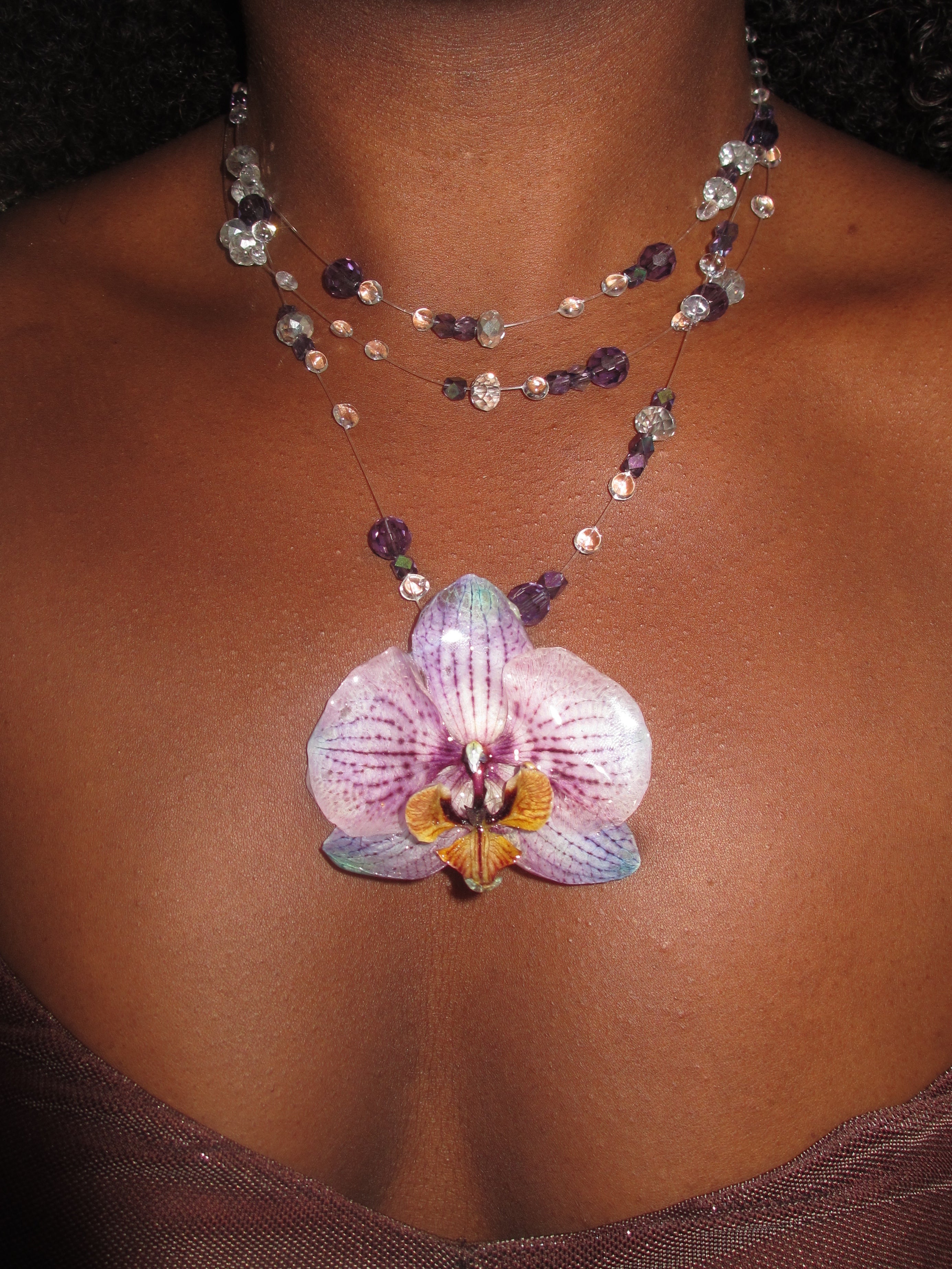 Ianthe preserved orchid necklace worn on model — real botanical pendant with crystal beads | smo studio - A close-up of a person's chest wearing a double-strand beaded necklace with a real purple orchid flower pendant.