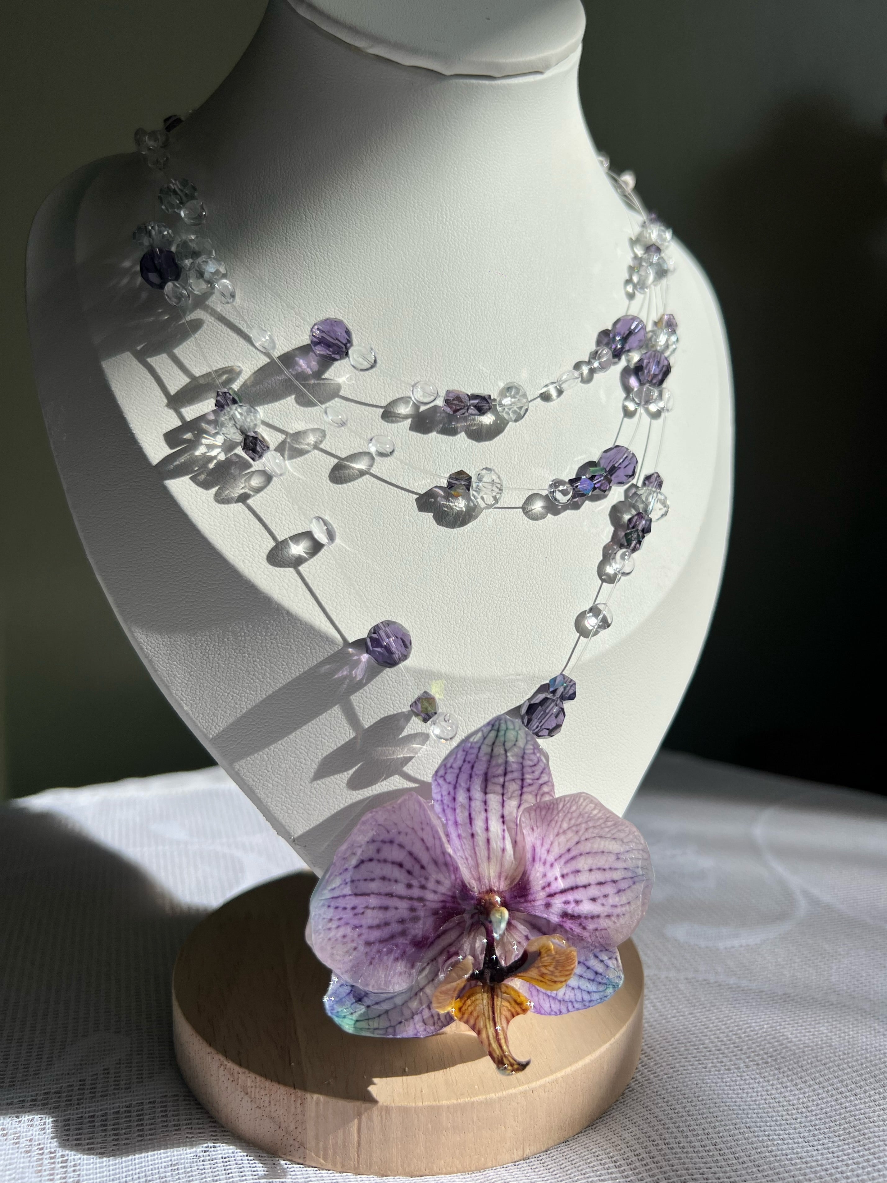 Ianthe crystal beaded necklace with real preserved orchid pendant — close-up detail | smo studio - A delicate beaded necklace with purple orchid pendant displayed on a white mannequin bust with a wooden base.